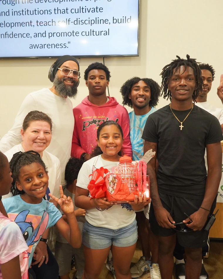 A group of children and teens pose together, one holding a decorated gift basket, with an inspirational quote displayed in the background.